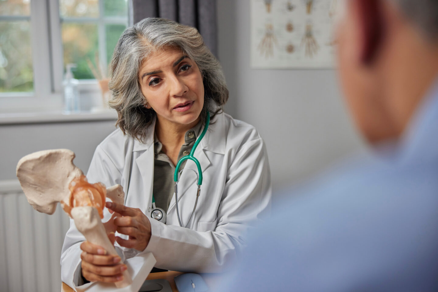 Mature Female Doctor Meeting With Male Patient to discuss PAO surgery and Joint Pain from hip dysplasia Using Anatomical Model