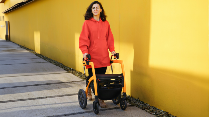 Young woman in an orange sweatshirt walks down the street with a walker